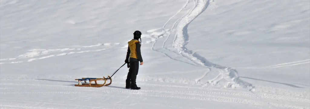 Eine Person zieht einen Schlitten über eine schneebedeckte Fläche, mit Fußabdrücken im Schnee.