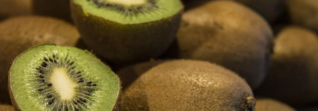 Eine geschnittene Kiwi zeigt das grüne Fruchtfleisch und die schwarzen Kerne, umgeben von ganzen Kiwis.