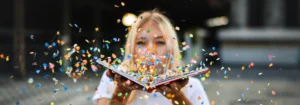 Eine Frau hält ein aufgeschlagenes Buch, während buntes Konfetti um sie herum fliegt.