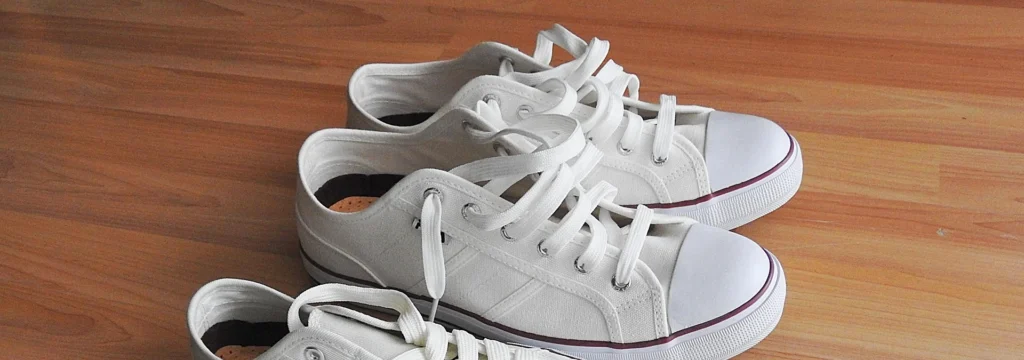 Zwei Paar weiße Sneakers mit langen Schnürsenkeln auf einem Holzboden.