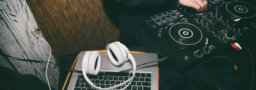 Weißer Kopfhörer auf einem Laptop neben einem DJ-Controller und einem Mischpult.