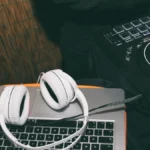Weißer Kopfhörer auf einem Laptop neben einem DJ-Controller und einem Mischpult.