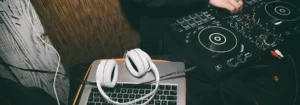 Weißer Kopfhörer auf einem Laptop neben einem DJ-Controller und einem Mischpult.