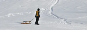 Eine Person zieht einen Schlitten über eine schneebedeckte Fläche, mit Fußabdrücken im Schnee.