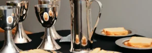 Silberne Kanne und Gläser auf einem Tisch mit Brotscheiben auf Tellern.